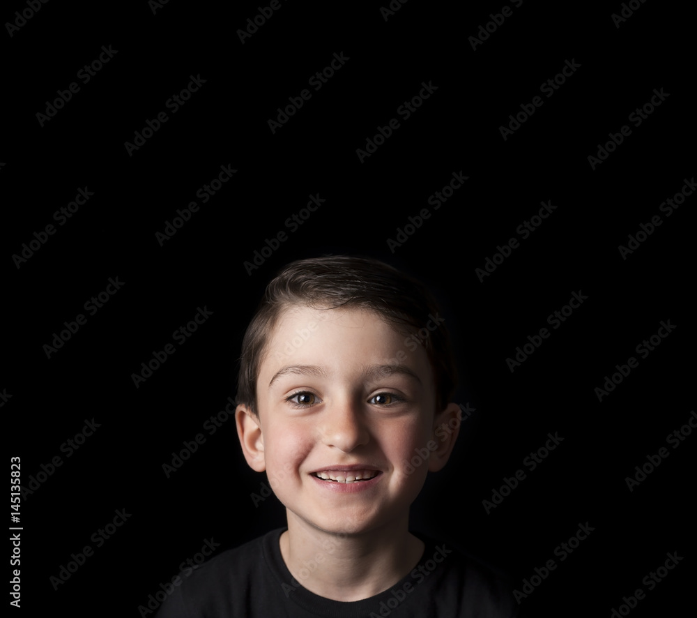 Low key portrait of young boy isolated on black background. Plenty