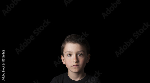 Low key portrait of young boy isolated on black background. Plenty of space left for copy. for Flyers, posters and other commercial purposes