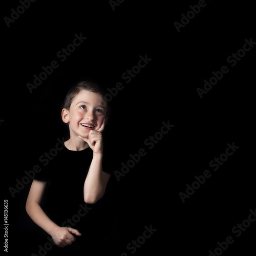 Low key portrait of young boy isolated on black background. Dreaming joyfully. .Plenty of space left for copy. for Flyers, posters and other commercial purposes