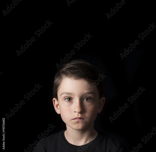 Low key portrait of young boy isolated on black background. Plenty of space left for copy. for Flyers, posters and other commercial purposes.Serious face