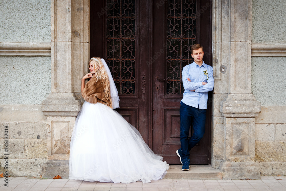 Beautiful young wedding couple stand happy together in a park in a white dress with a veil and a fur coat hugging a man and a woman together, young family, look lovingly at each other near castle