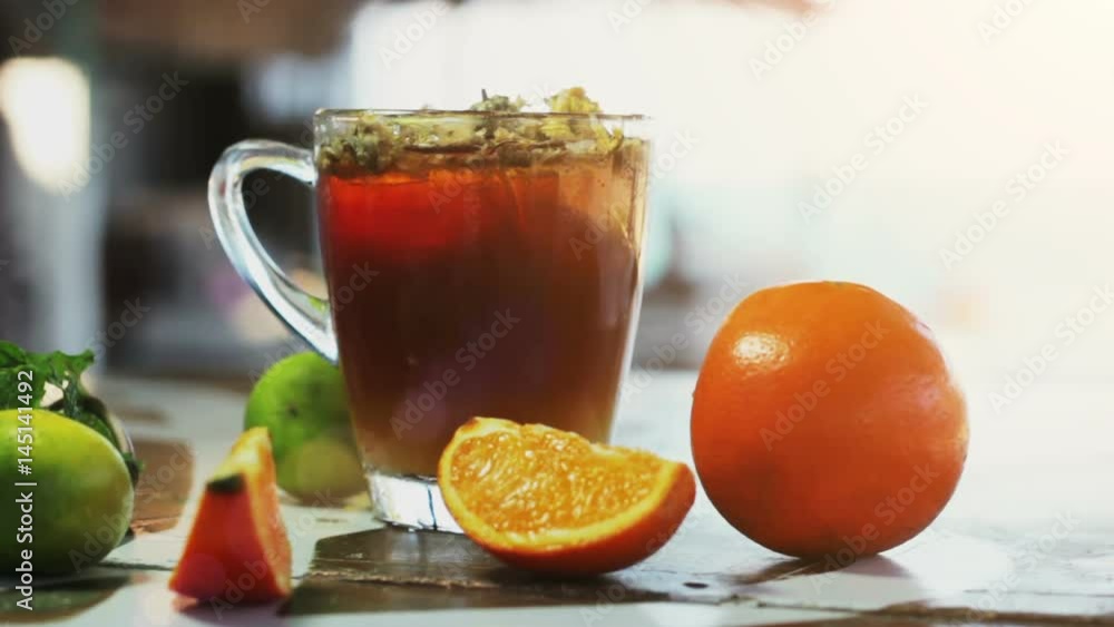 Glass of ice tea with сhrysanthemums and orange, ice cubes on dark wooden table on the sea background Glass of ice tea with сhrysanthemums and orange, ice cubes on dark wooden table on the sea background