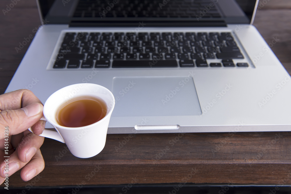 Open black laptop and hot cup of tea on wood table rad light Open black laptop and hot cup of tea on wood table rad light