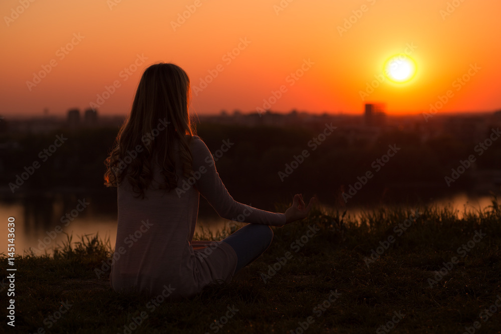Silhouette of a woman meditating at the sunset.