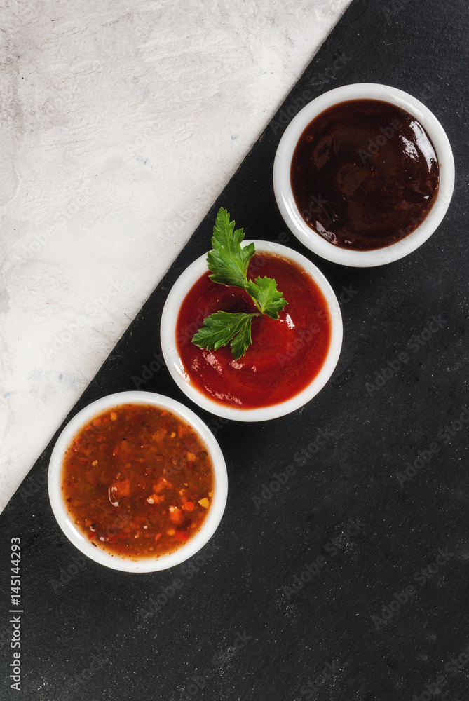 Three kinds of red tomato sauce on a white stone table: traditional classic ketchup, barbecue sauce, sweet and sour Chinese sauce. Top view copy space