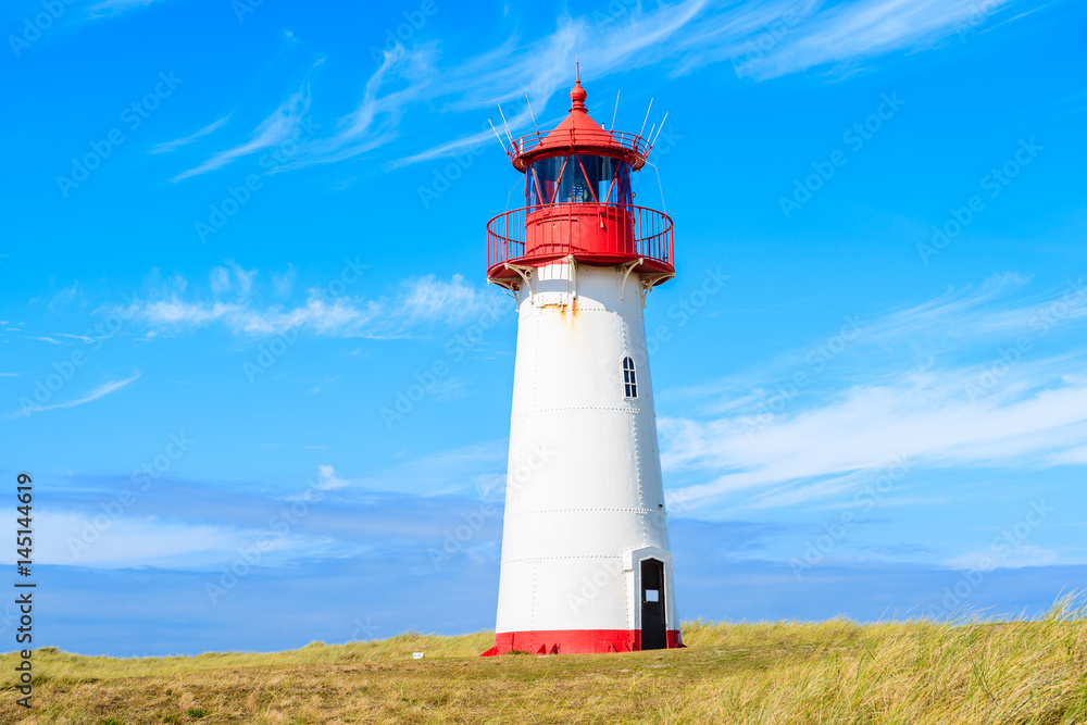 Lighthouse on sand dune against blue sky with white clouds on northern coast of Sylt island near List village, Germany