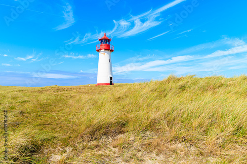 Lighthouse on sand dune against blue sky with white clouds on northern coast of Sylt island near List village, Germany