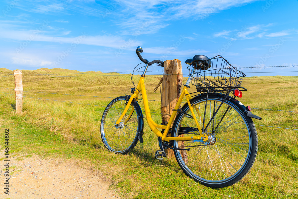 SYLT ISLAND, GERMANY - SEP 6, 2016: yellow bike parked against a field fence in countryside landscape of Sylt island near Ellenbogen beach, Germany. SYLT ISLAND, GERMANY - SEP 6, 2016: yellow bike parked against a field fence in countryside landscape of Sylt island near Ellenbogen beach, Germany.