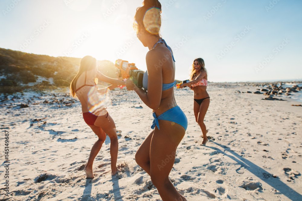 Three young women in bikini having water gun fight on beach foto de Stock |  Adobe Stock