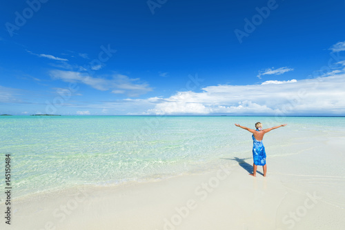 Rear view blonde woman with arms outstretched standing on the white sand beach.Copy space