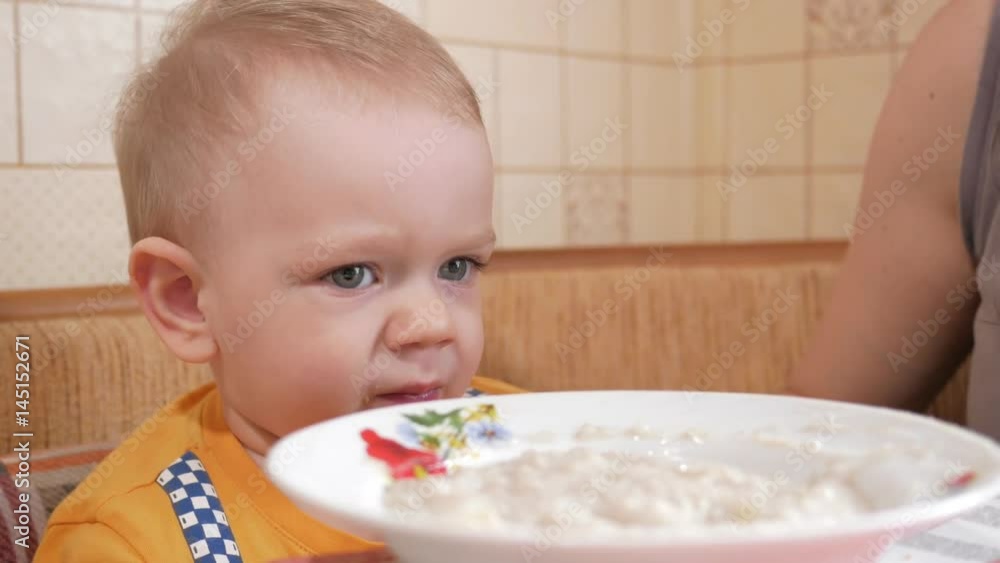Baby 2 years old eats porridge with a spoon. Mom sits next to the boy. home furnishings Baby 2 years old eats porridge with a spoon. Mom sits next to the boy. home furnishings