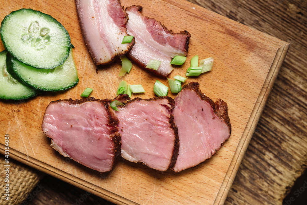 A close-up of sliced beef steak with a cucumber on a cutting board on a wooden background