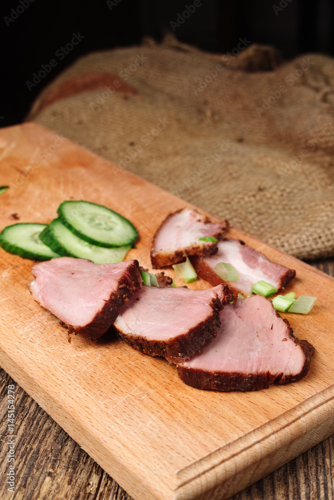 A close-up of sliced beef steak with a cucumber on a cutting board on a wooden background