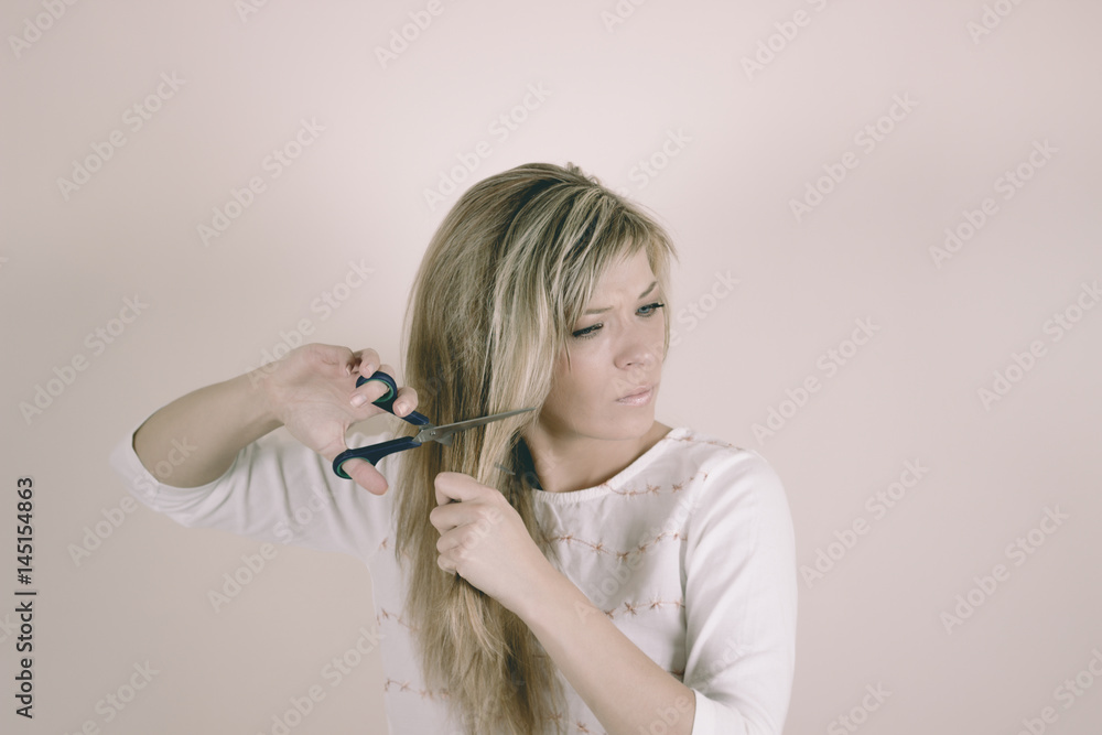 Obraz premium Angry blonde woman cuts her hair with scissors