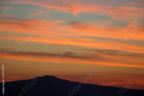 A top of mountain silhouette, under a big sky with beautiful, striped red clouds at sunset