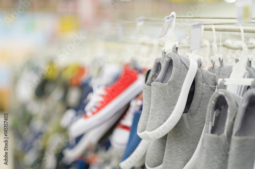 Rows of hangers with modern casual shoes of different colours in shoes store on blurry background