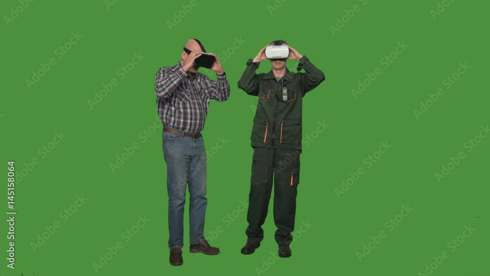 Two males in casual clothing putting on VR glasses and experiencing virtual reality isolated on green screen Two males in casual clothing putting on VR glasses and experiencing virtual reality isolated on green screen