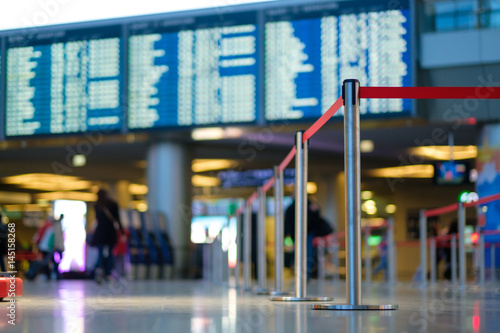 Stanchion barriers for waining lines in front of check in desks and flight schedule screens in airport on blurry background