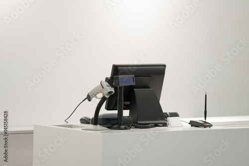 Cash desk with computer screen and barcode scanner on white table and wall in small store