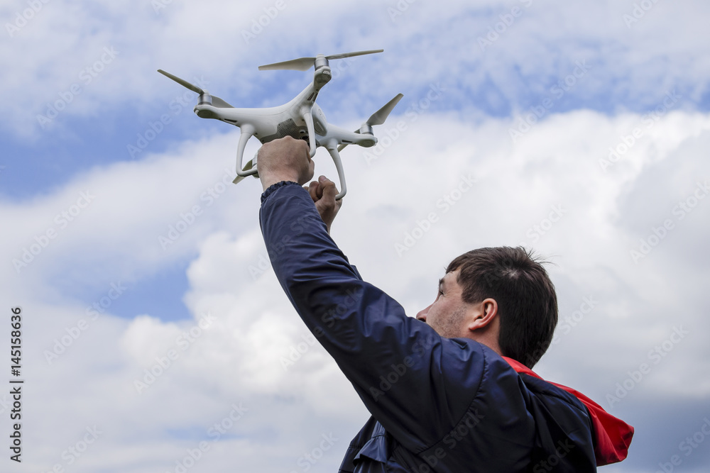 A man with a quadrocopter in his arms raised to the sky. A white drone is being prepared for the flight. A man with a quadrocopter in his arms raised to the sky. A white drone is being prepared for the flight.