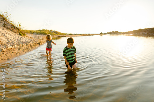 Girl and boy walking in water at sunset