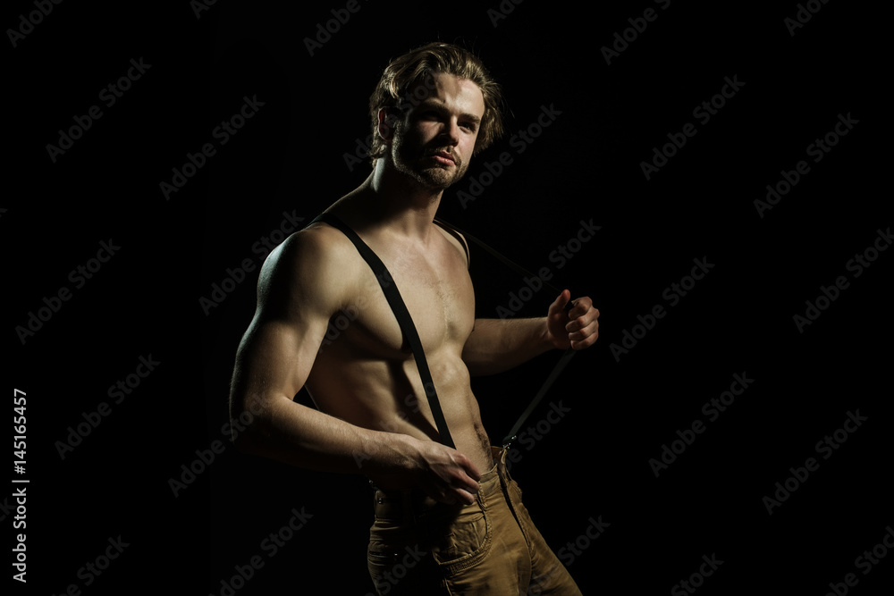 Sexy man is played with his suspenders for trousers on a black background. Seductive fashionable and sensual man