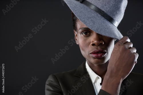 Androgynous man with hand on hat against grey background