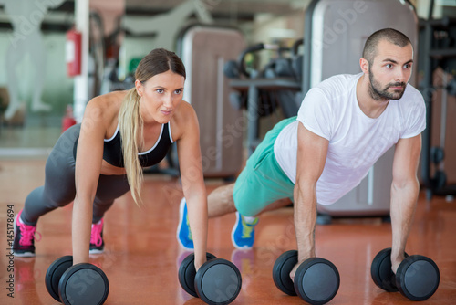 Fototapeta Naklejka Na Ścianę i Meble -  Gym man and woman push-up strength pushup with dumbbell in a workout
