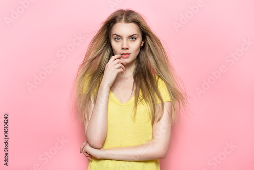 Beautiful woman with perfect face and natural makeup posing against pink wall wearing casual t-shirt.