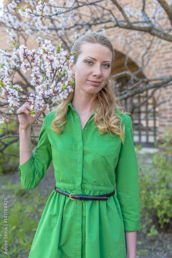 Fototapeta premium Young blonde girl on the background of a spring blooming garden