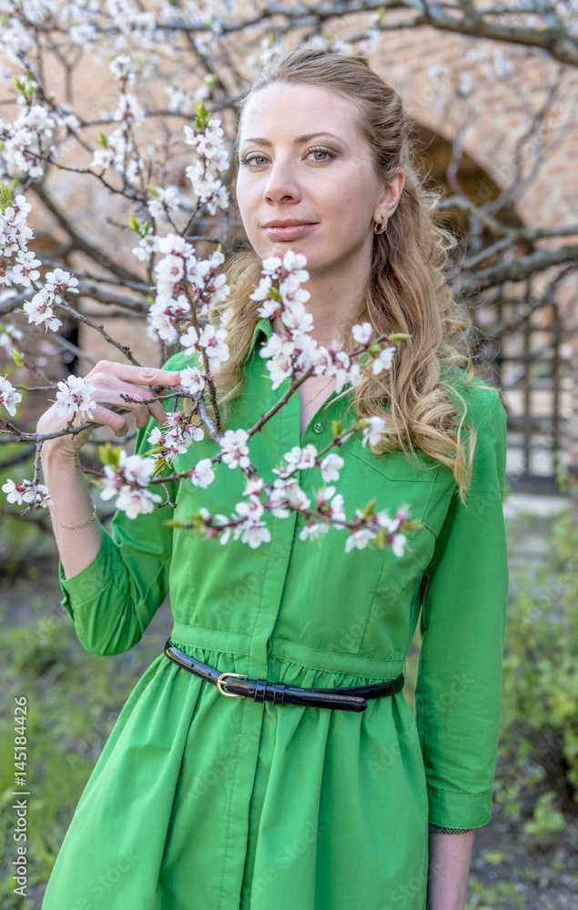 Fototapeta premium Young blonde girl on the background of a spring blooming garden