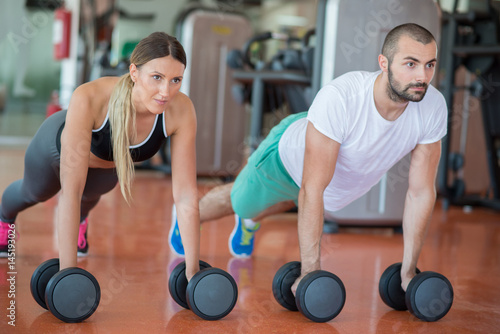 Gym man and woman push-up strength pushup with dumbbell in a workout