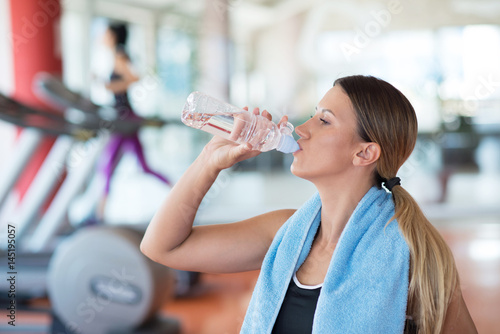 Fitness woman. Beautiful young girl in the gym drinking water, with blue towel.