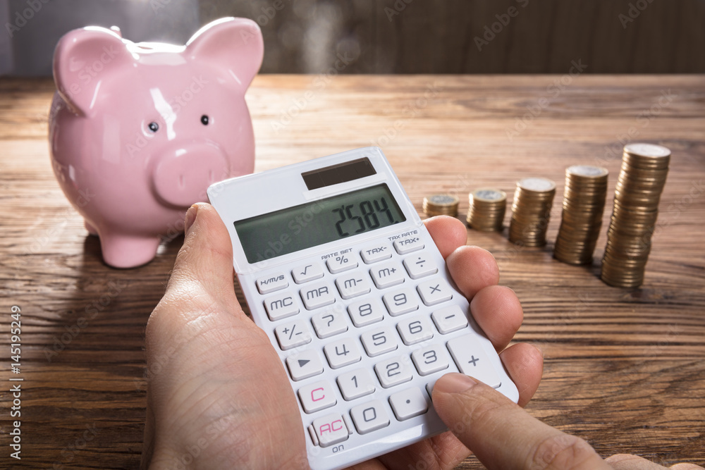 Person Calculating On Calculator With Piggybank And Coin Stacked Person Calculating On Calculator With Piggybank And Coin Stacked