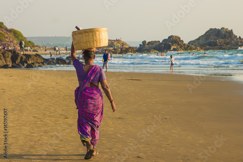 GOA, INDIA - MARCH 4: Woman in saris with basket on her head walks by Vagator beach on March 4, 2017 in Goa, India