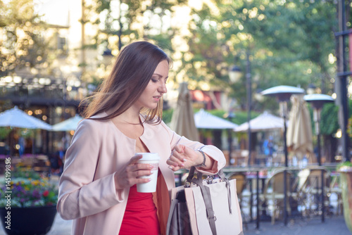 Young pretty woman checking time hurrying down city street
