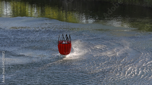 Detail of water bucket lifting out of the water under a helicopter with rotor wash on the surface of the lake