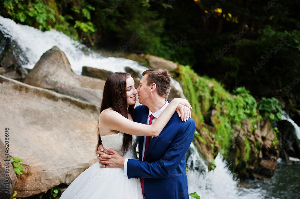 Lovely wedding couple against waterfall on sunset at Carpathian mountains.