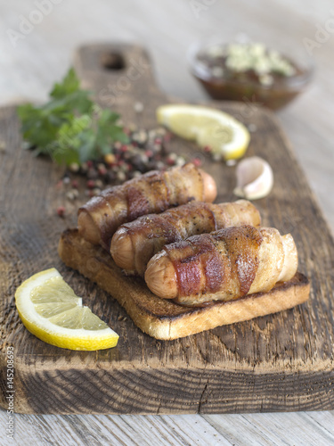 Fried sausages with bacon on a wooden board. 