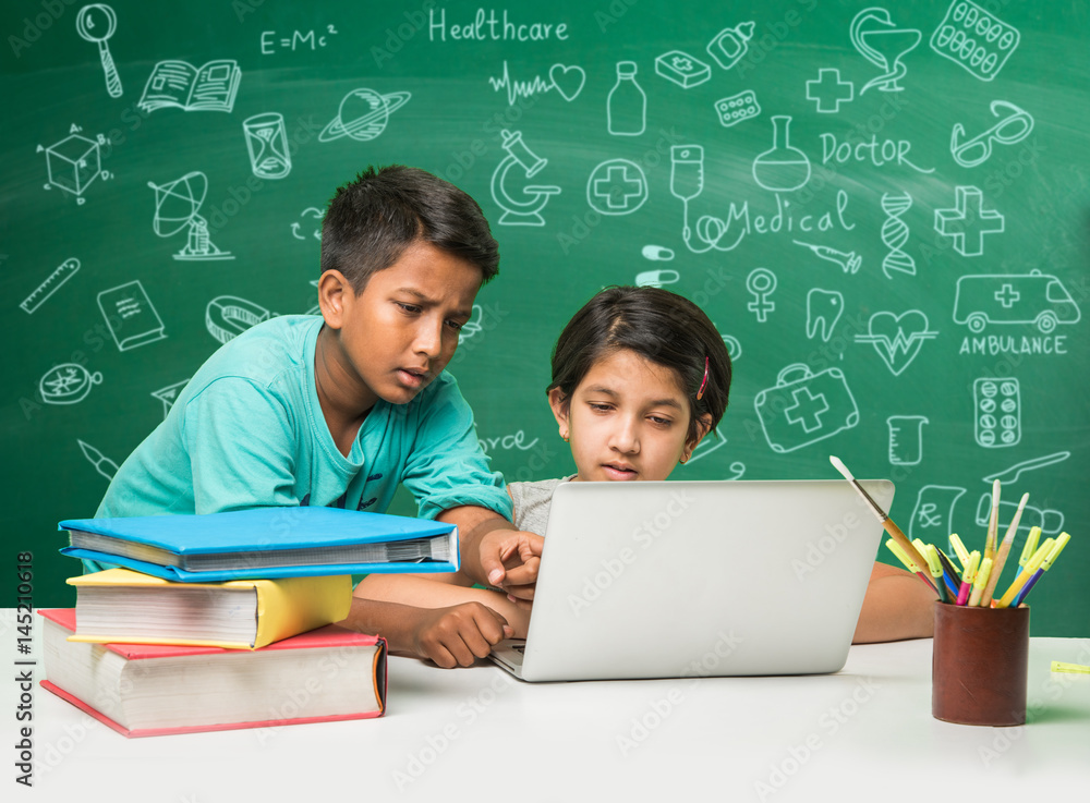 indian school kids using laptop in a classroom over green chalkboard ...