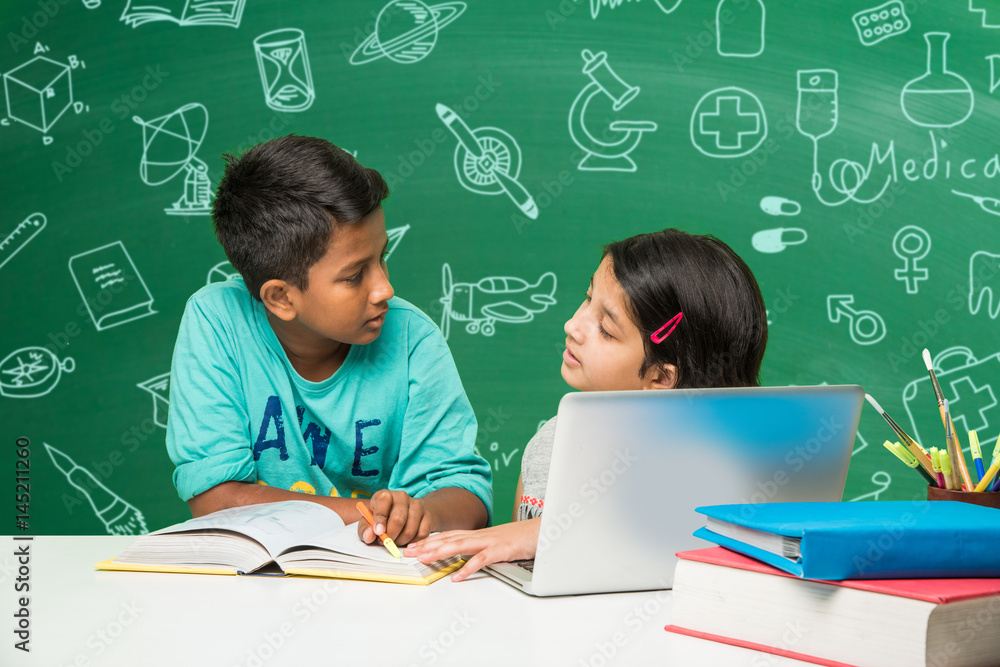 indian school kids using laptop in a classroom over green chalkboard ...