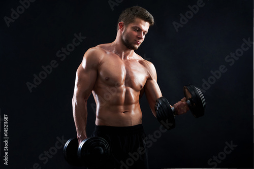 Horizontal studio shot of a young sexy male athlete exercising with heavy weights on black background posing shirtless showing off his hot toned ripped body confidence masculinity ambition motivation.