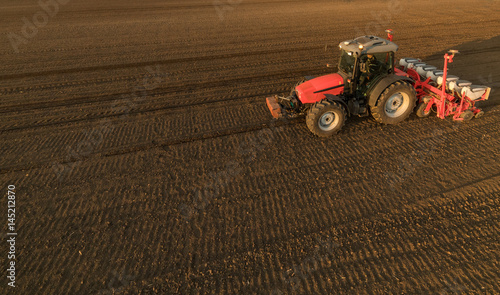 Farmer with tractor seeding - sowing crops at agricultural field in spring