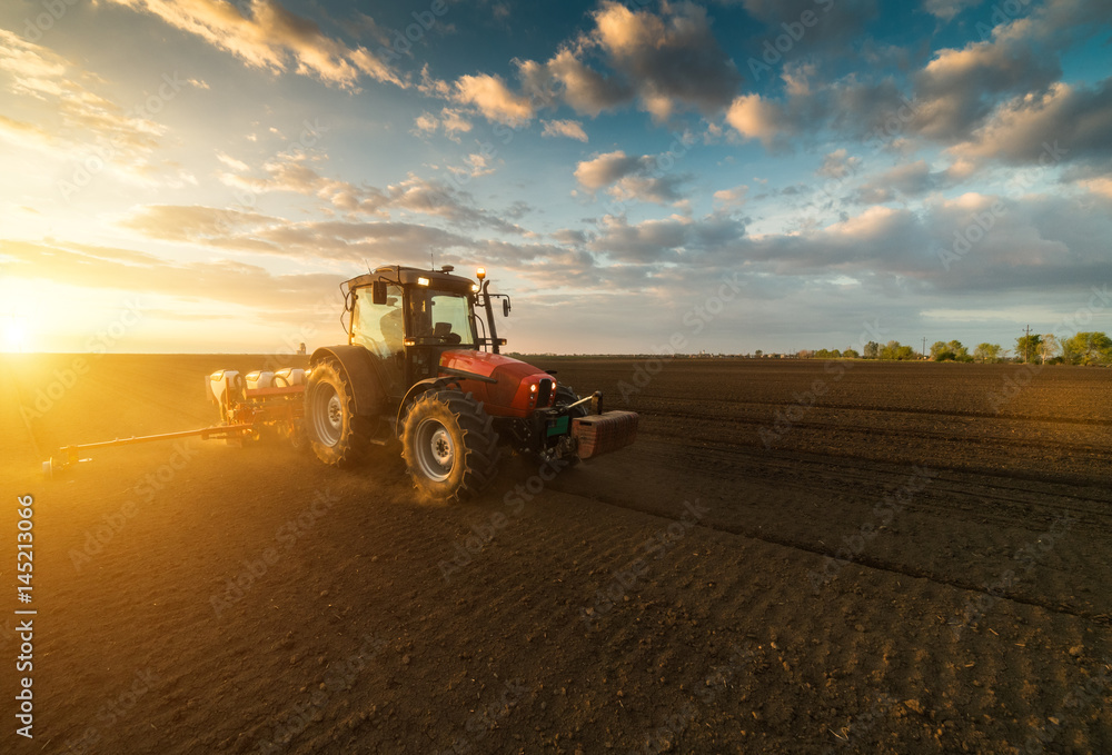 Farmer with tractor seeding - sowing crops at agricultural field in spring Farmer with tractor seeding - sowing crops at agricultural field in spring