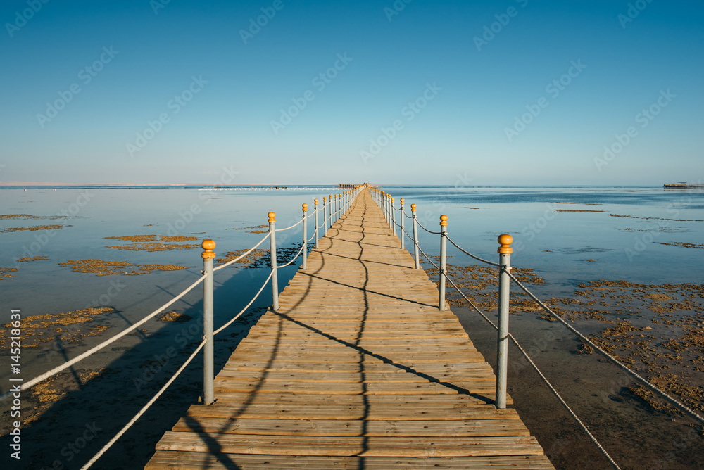 Pier in the Red sea in resort. Summer vacation on Red sea. View at a clear sea with turquoise water in windless conditions. Summer vacation at a sea coastline in an exotic country.