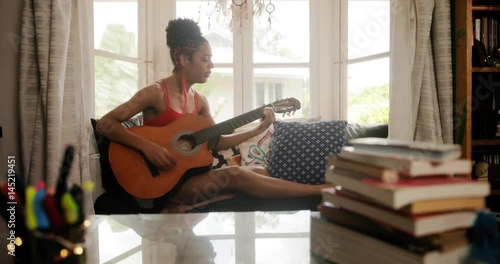 Black girl lying on couch and singing song, young african american woman relaxing. Happy latina sitting on sofa and playing guitar. Music, leisure and relaxation at home
