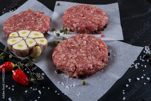 Fresh raw meat burger cutlet on the black slate board with herbs and spices for background.  top view ..