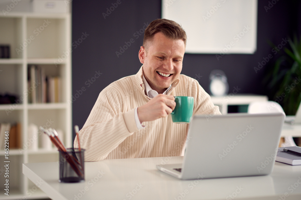 Young handsome man working in modern office sitting at the table with laptop