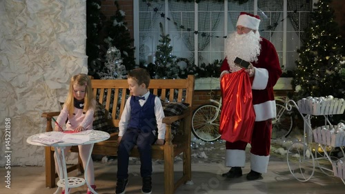 Santa Claus Gives Present to Boy Girl is Drawing at the Table People in Cosy Well Decorated Modern Room Animator Entertains Kids Christmas New Year Lights