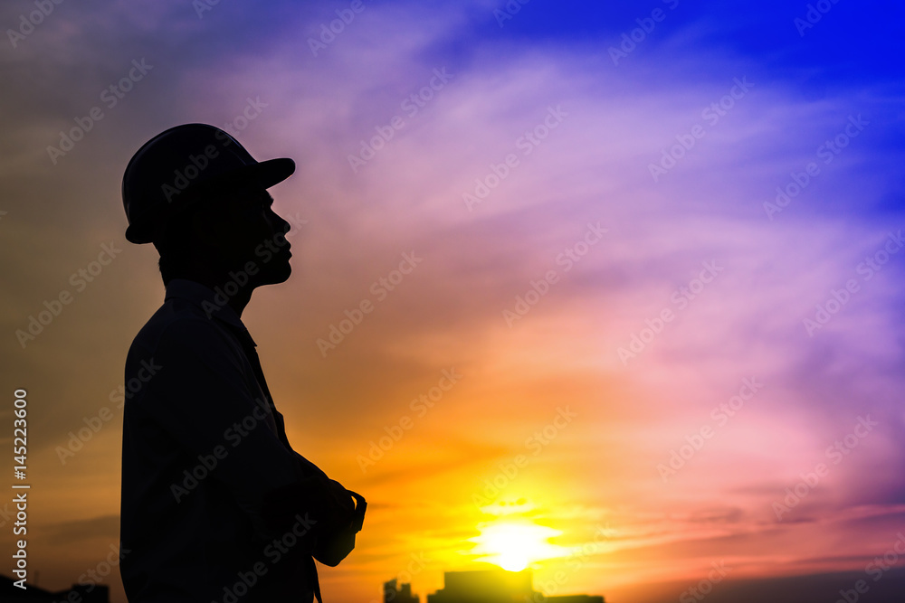 portrait of architect silhouette wear a helmet at construction site with crane background and sunset